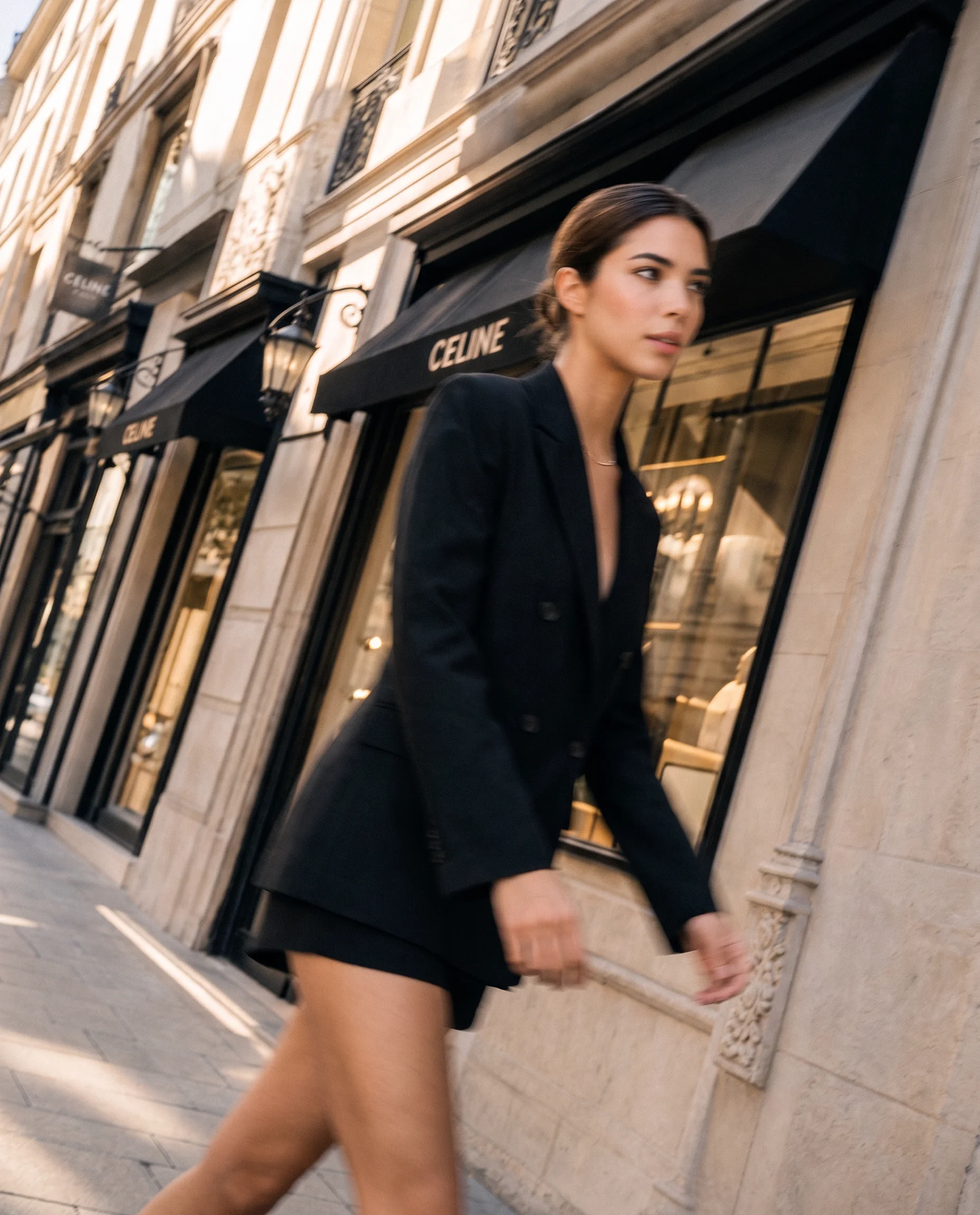 Pera in a black tailored blazer and mini skirt walking past a Paris storefront